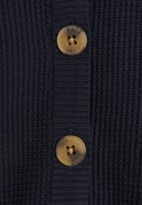 Cardigan in tessuto navale con due bottoni trasparenti e marchio inciso, che presenta un motivo a maglia a coste e una leggera lucentezza.