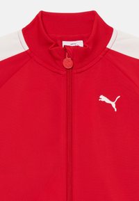 Czerwona kurtka dresowa na zamek z wysokim kołnierzem, białymi akcentami na ramionach i białym logo Puma na klatce piersiowej. Gładki, elastyczny materiał.