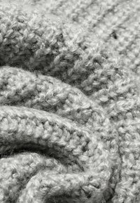 Primer plano de una suave y ligera tela de lana gris claro tricotada, mostrando detallados puntos de textura y suaves pliegues.