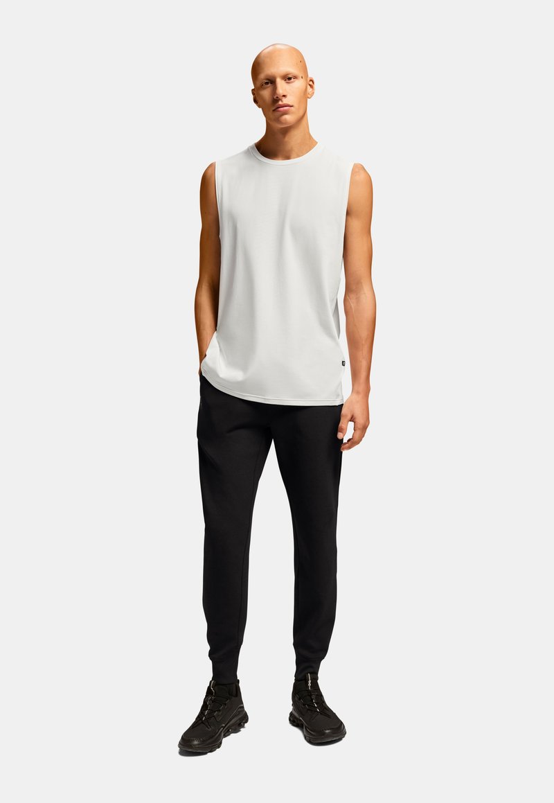 Hvid ærmeløs t-shirt parret med sorte tætsiddende bukser og sorte sportssko, med en glat tekstur og minimalistisk design.