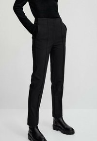 Black tailored pants with a high waist, side pockets, and front seam detailing, paired with chunky black ankle boots.