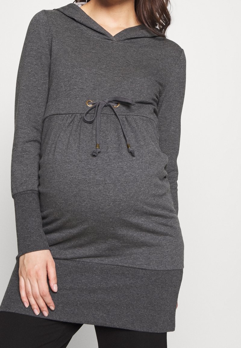 Šedý tunikový svetr s kapucí, dlouhými rukávy, stahováním v pase a žebrovaným lemem. Vyrobený z měkké látky, navržený pro pohodlný střih přes těhotenské bříško.