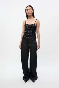 Μαύρο αμάνικο τοπ με ρυτιδωτή σχεδίαση και διακοσμητικά λουλούδια, σε συνδυασμό με μαύρο τζιν παντελόνι φαρδιάς γραμμής και τακούνια με μυτερή μύτη.