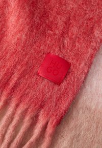 Wool scarf in gradient shades of red, featuring a textured finish and fringe edges. A red tag with embossed "HUGO" logo is present.