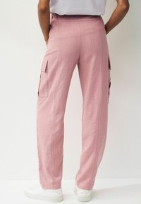 Roze cargobroek gemaakt van lichtgewicht stof, met zijzakken, een ontspannen pasvorm en een elastische tailleband. Gestyled met witte sneakers.