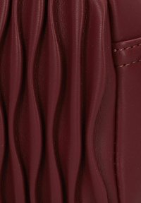 Burgunderfarbene Lederhandtasche mit strukturierten, wellenförmigen Falten und glatten Abschnitten, geprägt von präziser Nahtführung und einer klaren Form.