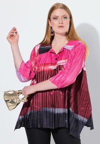 Camicia con bottoni caratterizzata da pieghe verticali in tonalità di rosa, rosso e nero. Maniche corte e colletto a punta. Abbinata a una borsa dorata.