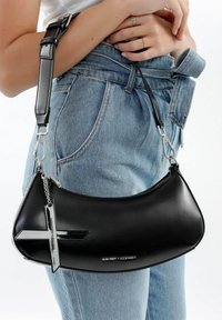 Borsa a tracolla in pelle nera con forma curva, chiusura a zip, hardware argentato e un pendente a croce decorativo. Tracolla regolabile con fibbia.