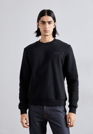 Black sweatshirt with a crew neck, ribbed cuffs, and hem. Features subtle branding on the chest. Paired with dark denim jeans.