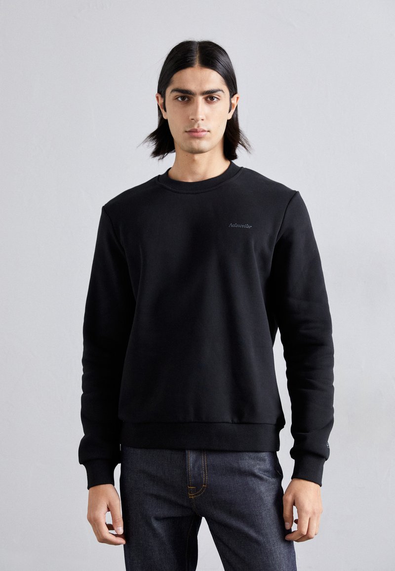 Sort sweatshirt med rund hals, ribbede ærmer og kant. Har subtile branding på brystet. Sammen med mørke denim jeans.