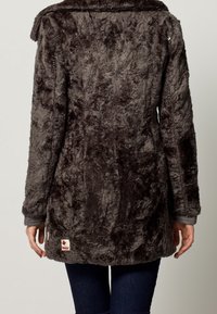 Abrigo de piel sintética en gris oscuro con una textura suave, que presenta un cuello ancho y un parche bordado con el logo en el dobladillo. La tela se ajusta al cuerpo de manera cómoda.