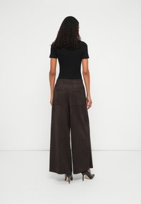 Pantaloni largi, cu talie înaltă, de culoare maronie, realizați dintr-un material moale, având două buzunare la spate și un brâu elastic, asortați cu tocuri negre.