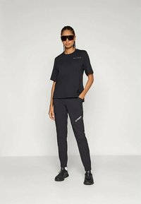 Conjunto atlético preto composto por uma t-shirt larga e calças justas, ambas com um logotipo discreto, combinadas com ténis pretos e óculos de sol.