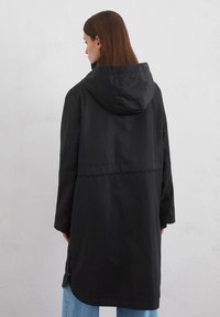 Veste à capuche noire au design droit, dotée d'une taille élastique, de fentes sur les côtés et d'une texture lisse et mate.