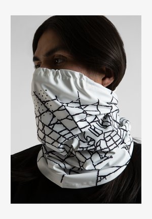 Valkoinen kaulahuivi pehmeästä kankaasta, jossa on musta geometrinen kuvio, jossa on pisteitä. Muotoiltu aukko mahdollistaa helpon pukemisen.