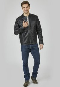 Svart läderjacka för män med dragkedja framtill, stående krage och sidofickor, matchad med blå jeans och bruna stövlar.