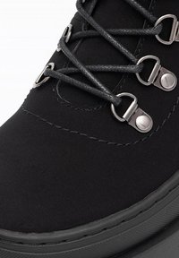 Čierne semišové čižmy s metalickými očkami a čiernymi šnúrkami. Majú hladký povrch, zaoblenú špičku a hrubú gumovú podrážku.