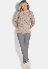 Lichtroze top met diamantpatroon in blauw en bruin, driekwartmouwen, gecombineerd met grijze broek en witte sneakers. Soepele textuur.