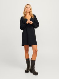 Schwarzes gestricktes Kleid mit V-Ausschnitt, langen Ärmeln und lockerer Passform, kombiniert mit knielangen schwarzen Lederstiefeln.