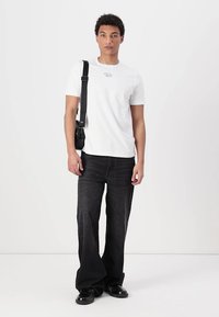 Hvid bomulds t-shirt med en lille grafik på brystet, parret med løstsiddende sorte denim-bukser og sorte sko.