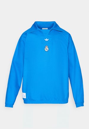 Zils garām piedurknēm puloveris ar punktētu apkakli. Uz krūtīm izšūts Adidas logotips un Real Madrid ģerbonis. Elastīgas aproces.