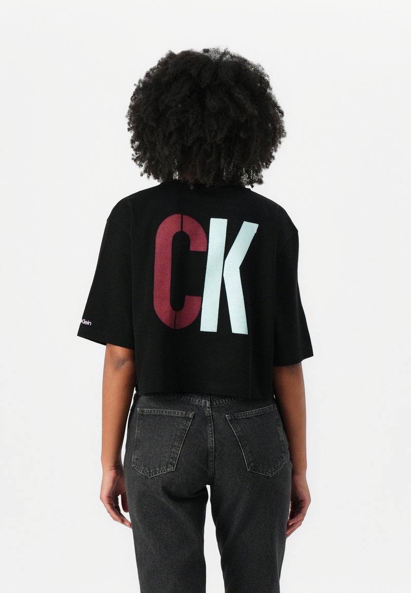 Juodas trumpas marškinėliai su dideliu "CK" logotipu raudonai ir šviesiai mėlynai ant nugaros. Pagaminti iš minkštos medvilnės, su trumpomis rankovėmis ir laisvu siluetu.