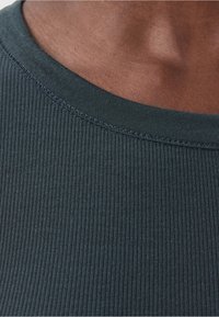 Tessuto a maglia a coste di colore verde scuro, caratterizzato da una ampia scollatura a girocollo e cuciture visibili che mettono in risalto la sua texture e il design.
