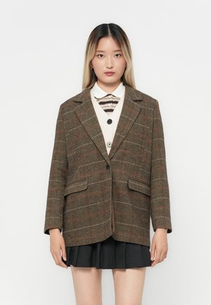 Brown herringbone-patterned blazer with two front pockets, notched lapels, and a single black button, worn over a white and striped shirt.