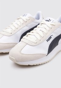 Zapatillas blancas y marinas con materiales de ante y malla. Presentan cordones, suela de goma y detalles del logo lateral. Diseño de punta redondeada.