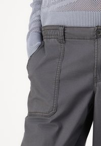 Gray cargo pants with side pockets, made of durable fabric. Features stitching details and a button closure at the waist.