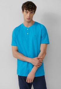 Türkises Kurzarm-Henley-T-Shirt mit Rundhalsausschnitt, zwei-Knopf-Leiste und dezentem Branding auf der Brust; glatte Stofftextur.