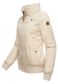 Veste zippée beige clair avec col haut, poignets et ourlet côtelés, fermeture éclair à l'avant, poches latérales et écussons de marque sur la poitrine et la manche.