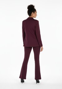 Bordowy garnitur z dopasowaną marynarką i rozszerzanymi spodniami. Gładka tkanina, mankiety zapinane na pojedynczy guzik oraz dopasowany krój.
