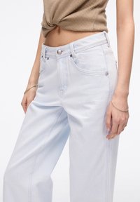 Jeans de mezclilla azul claro con un ajuste holgado, que presentan una cintura alta, cierre de botón y dos bolsillos frontales. Textura pronunciada y costuras sutiles.