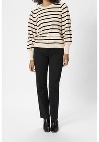 Cremefarvet sweater med sorte vandrette striber, puffede ærmer og ribbede manchetter, parret med sorte lige bukser og sorte ankelstøvler.