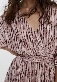 Wrap dress featuring soft, lightweight fabric with a pink and maroon abstract pattern, v-neckline, and smocked waist detail.