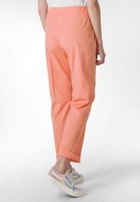 Pantaloni leggeri color corallo con una vestibilità morbida, gambe svasate e una cintura elastica. Presentano una cucitura discreta e nessuna tasca visibile.