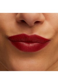 Rote Lippenstift auf vollen Lippen, der ein glattes und glänzendes Finish präsentiert. Die Hauttextur wirkt natürlich und makellos.