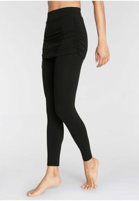 Zwarte legging met een hoge taille en een geplooid detail bij de taille. Glad, elastisch materiaal reikt tot de enkel. Geen zichtbare patronen of hardware.
