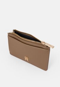 Vaaleanruskea nahkato Wallet, jossa on kultaisen sävyinen vetoketju, kohokuvioitu logo ja musta sisävuori. Kompakti muotoilu, jossa on yksi vetoketjullinen lokero ja korttipaikat.