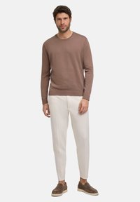 Brauner Strickpullover mit Rundhalsausschnitt, kombiniert mit weißen Hosen und braunen Slippern. Das Ensemble ist modern und figurnah.