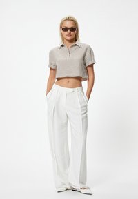 Camisa recortada de rayas en beige y blanco con cuello; pantalones blancos de pierna ancha y cintura alta; gafas de sol negras elegantes; ajuste relajado.