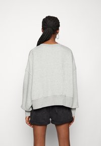 Sudadera gris de gran tamaño con hombros caídos, dobladillo acanalado y puños. Combinada con pantalones cortos de mezclilla negros, con dobladillos enrollados.