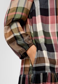 Geruite jurk met multicolor patronen in tinten roze, groen, bruin en zwart; elastische mouwen met geplooide accenten en zijzakken.