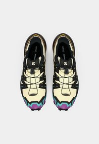 Des chaussures de sport multicolores avec un dessus crème, des accents noirs, des détails violets et turquoise, et une semelle texturée pour l'adhérence.