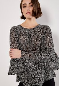 Transparante zwarte blouse met witte bloem- en geometrische patronen. Ronde hals, lange flared mouwen en een ontspannen pasvorm. Zacht, lichtgewicht stof.