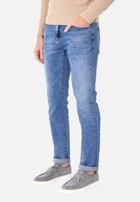 Jeans in denim blu chiaro con una vestibilità slim, caratterizzati da un lavaggio sbiadito, leggere sfumature e risvolti. Abbinati a sneaker in suede grigio.