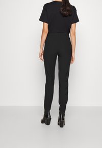 Czarne dopasowane spodnie o zwężanym kroju, wykonane z gładkiego materiału. Noszone z czarną koszulą z krótkim rękawem i botkami za kostkę.