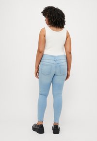 Light blue skinny jeans with a high waist and back pockets, paired with a fitted white tank top and platform shoes with studs.