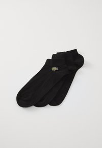 Chaussettes noires de cheville en matériau doux, avec un petit logo de crocodile brodé vert et rouge sur le côté. Quatre paires empilées.